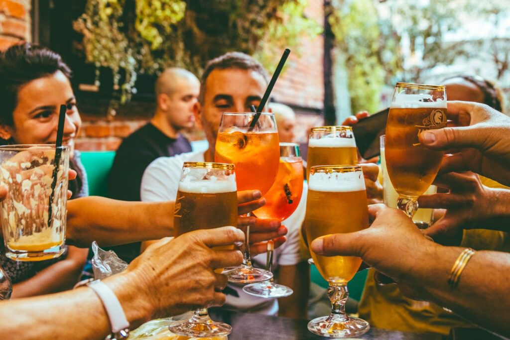 Freunde stoßen mit Bier und Cocktails im sonnigen Biergarten an. Foto: Fred Moon / Unsplash