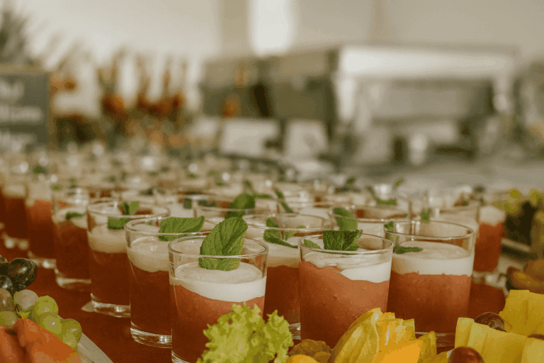 Rote Grütze mit Vanillesoße im Glas, garniert mit Minze, auf Dessertbuffet mit frischen Früchten
