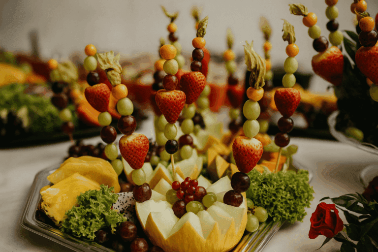 Dekorative Obstplatte mit Fruchtspießen, Erdbeeren, Trauben und Melone für festliches Catering