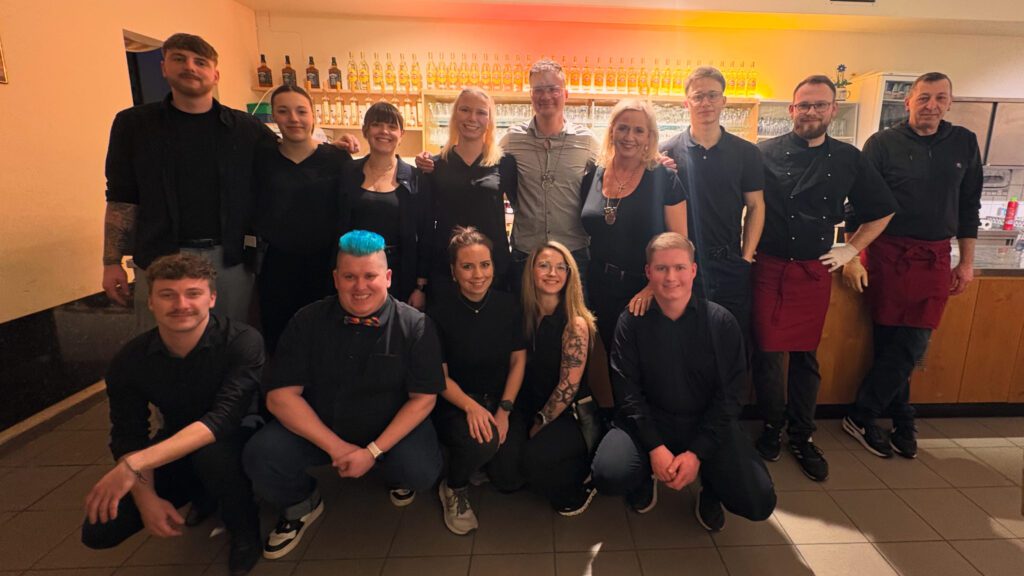 Professionelles Gastronomie-Team posiert vor beleuchteter Bar mit Spirituosenregal